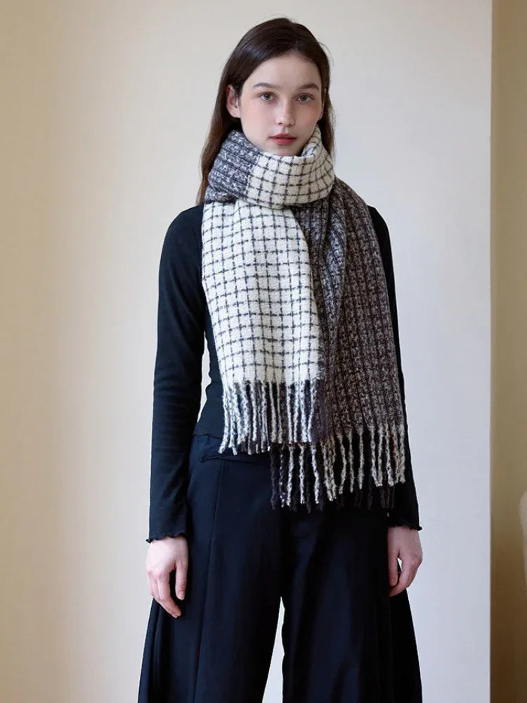Woman wearing a black long-sleeve top and a plaid scarf with fringe detail, styled loosely around her neck.