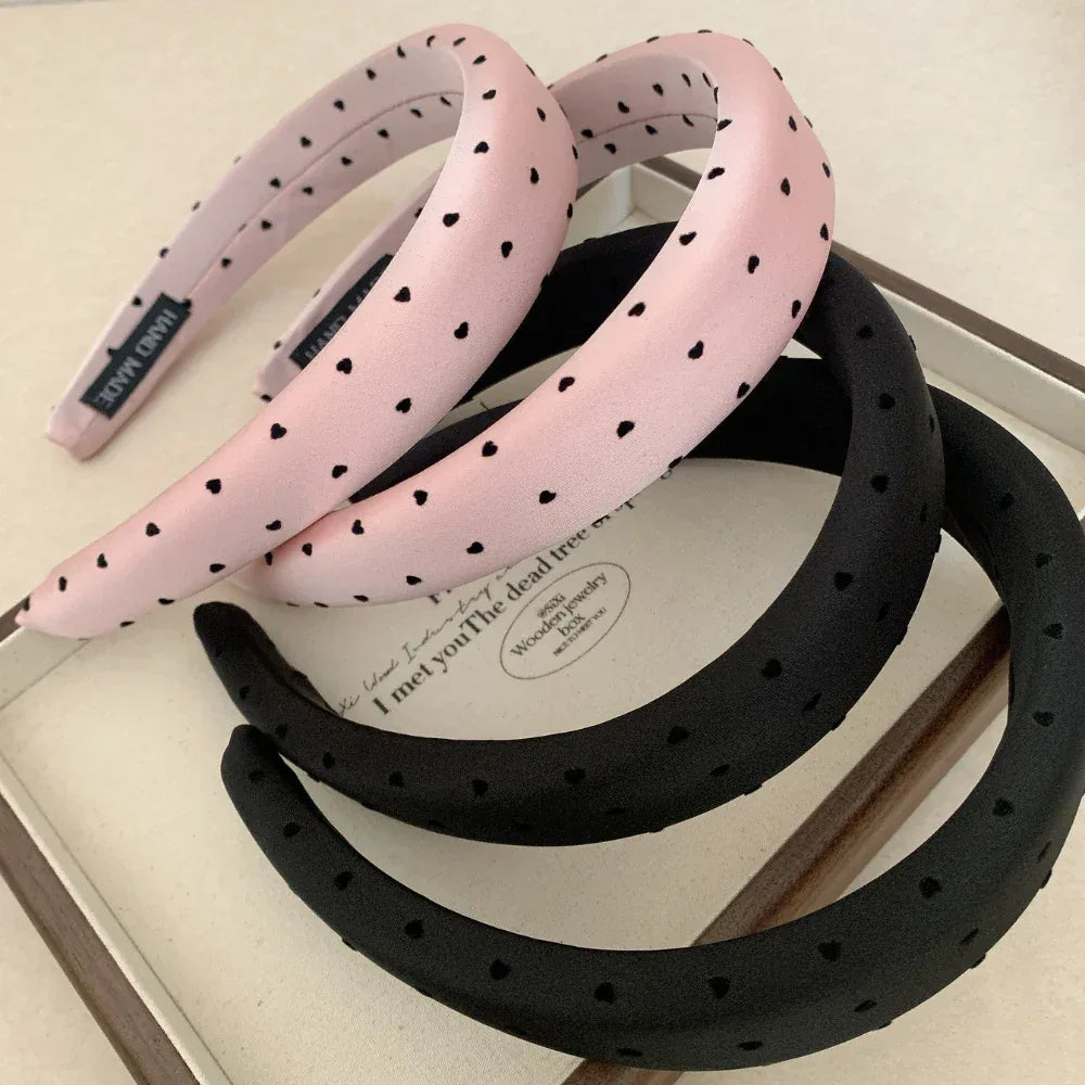 A group of pink and black puffy headbands with heart prints arranged on a surface.