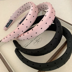 A group of pink and black puffy headbands with heart prints arranged on a surface.