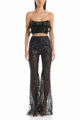 Woman wearing a black sequined two-piece outfit with feather trim and flared pants, front view.