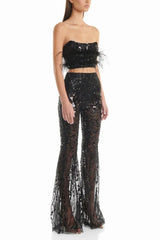 Woman wearing a black sequined two-piece outfit with feather trim and flared pants, side view.