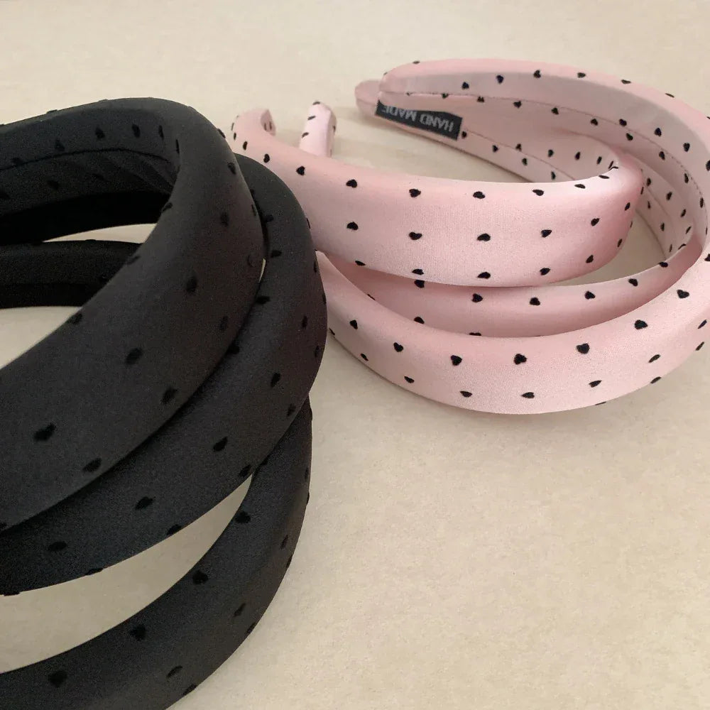 Close-up view of stacked black and pink puffy headbands with heart prints.