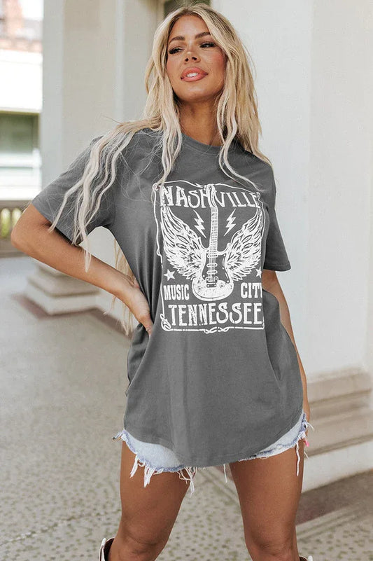 Woman wearing a grey graphic t-shirt with 'Nashville Music City Tennessee' and a guitar with wings design, paired with denim shorts.