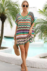 Woman wearing a colorful striped crochet knit tunic with a v-neck and short sleeves, holding a straw hat and standing by a pool.