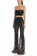 Woman wearing a black sequined two-piece outfit with feather trim and flared pants, three-quarter view.