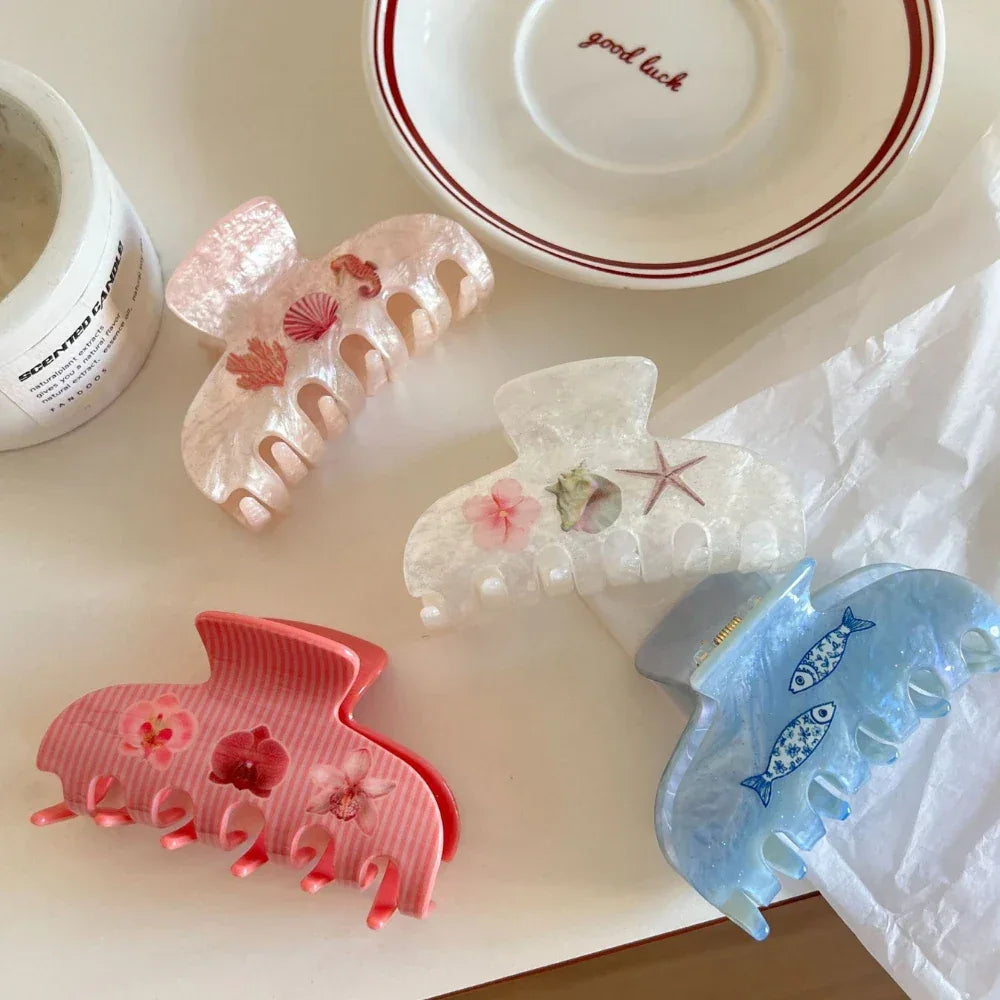 Collection of four decorative claw clips in pink, white, and blue with oceanic and floral designs