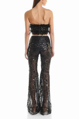 Back view of a woman wearing a black sequined two-piece outfit with feather trim and flared pants.