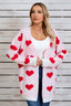 Woman wearing a pink longline cardigan with a red heart print, a white tank top, and blue jeans.