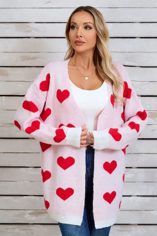 Woman wearing a pink longline cardigan with a red heart print, a white tank top, and blue jeans.