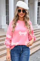 Woman wearing a pink knit sweater with a light pink bow pattern and blue jeans
