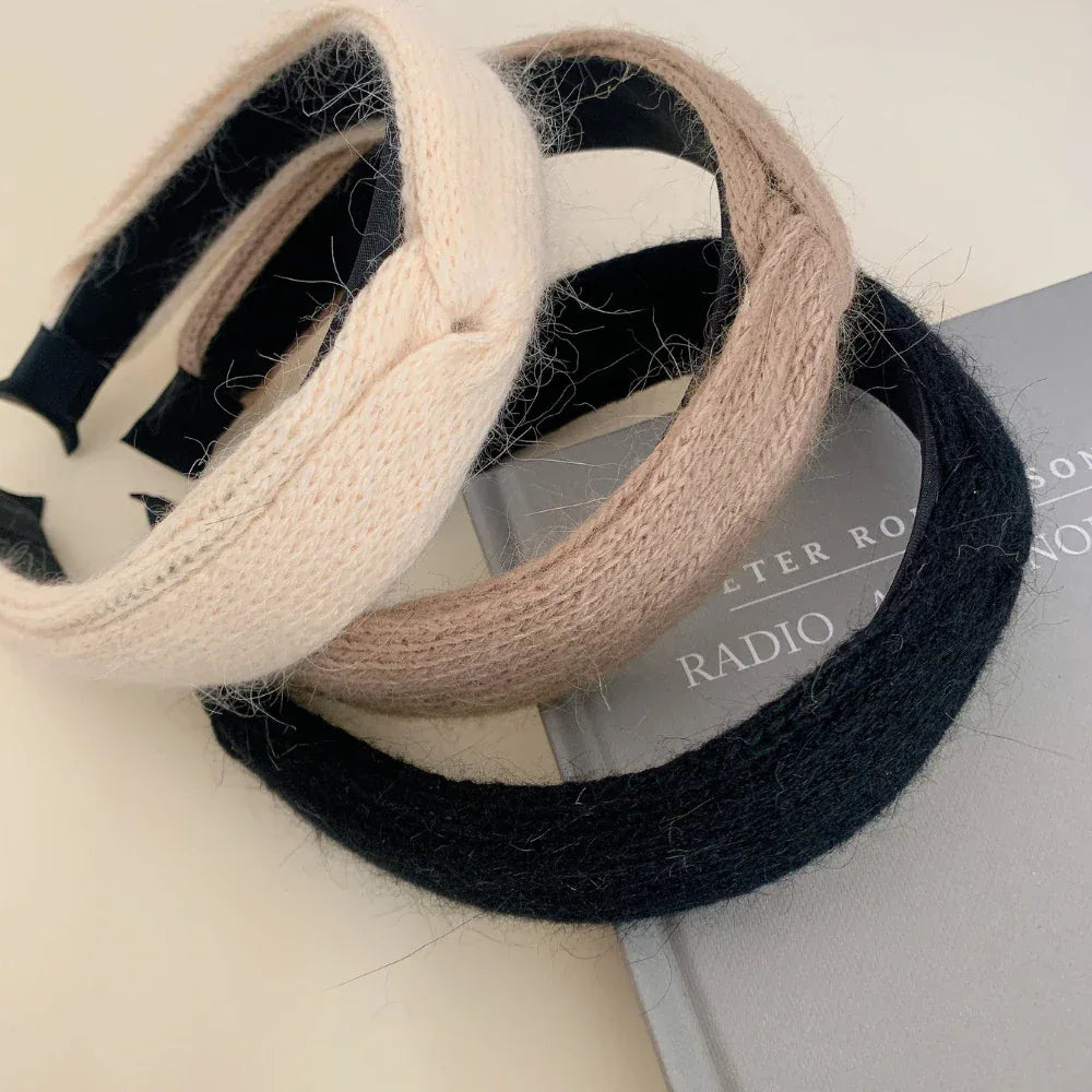 Three knit headbands in cream, taupe, and black arranged on a book
