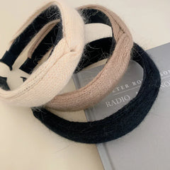 Three knit headbands in cream, taupe, and black arranged on a book