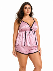 Front view of a pink satin cami and shorts pajama set with black heart print and lace trim, showing the v-neckline and bow.