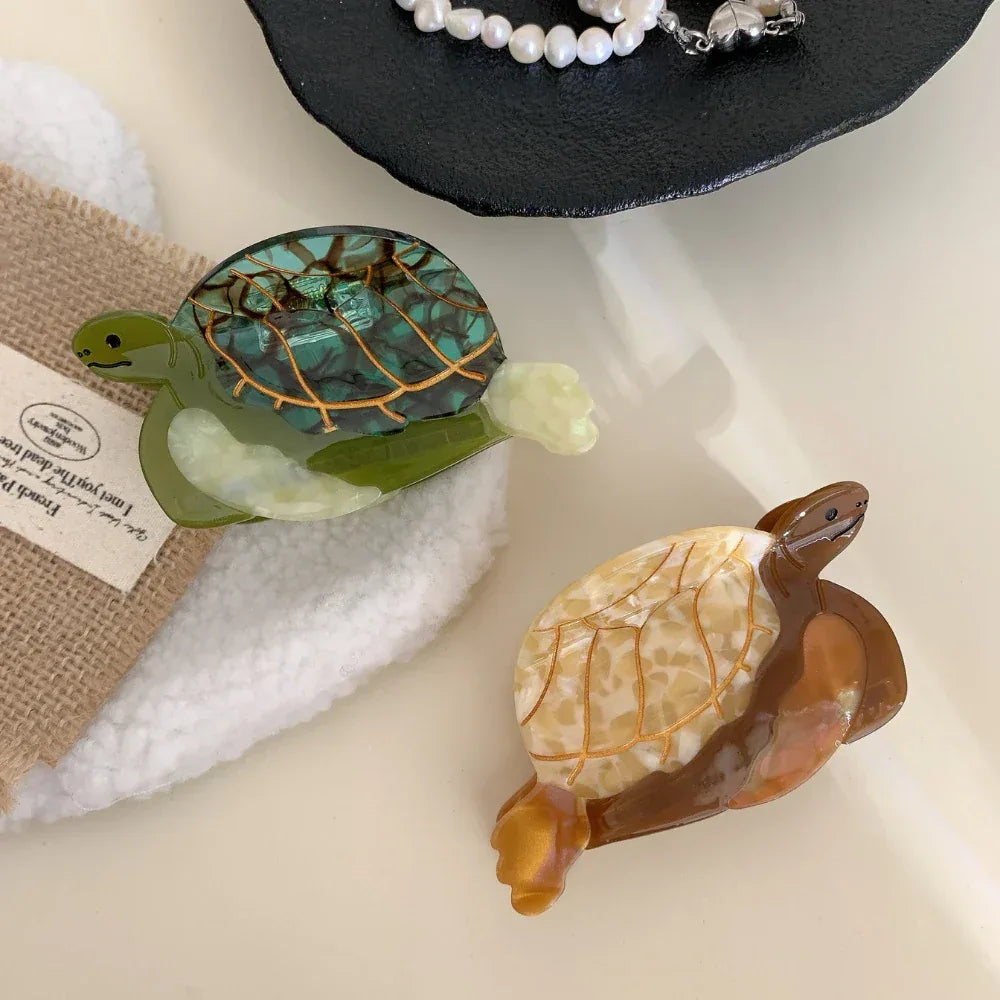 Close-up of a green acetate turtle hair clip and a brown/tan acetate turtle hair clip with pearl necklace in the background