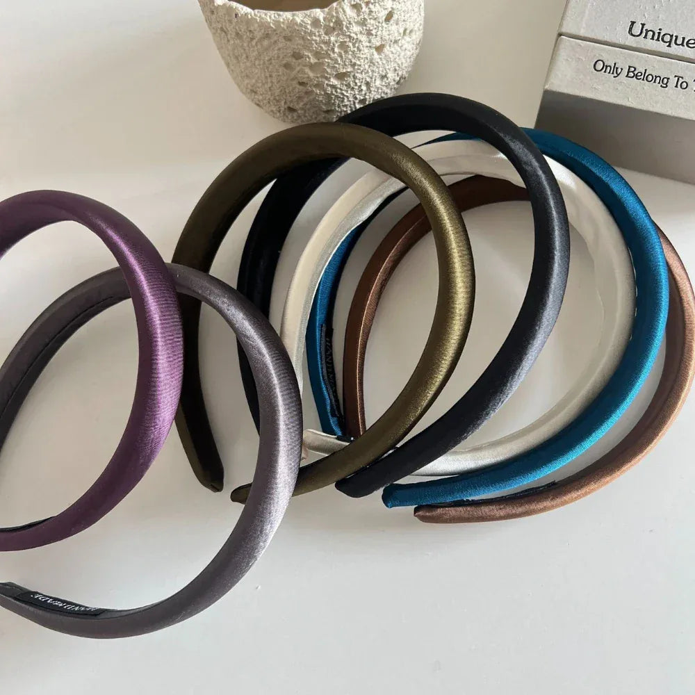 Close-up of multiple padded satin headbands in different colors arranged on a white surface