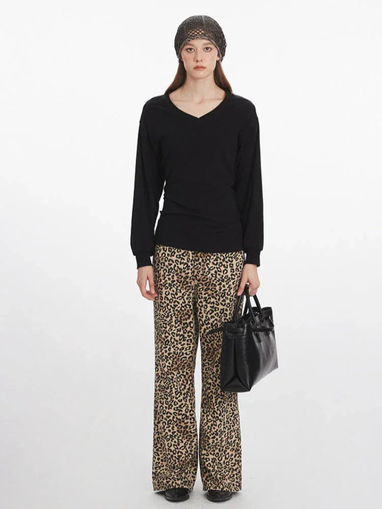 Woman wearing a black V-neck long-sleeved top, leopard print wide-leg pants, a grey knit beanie, and carrying a black structured handbag, shown from the front.