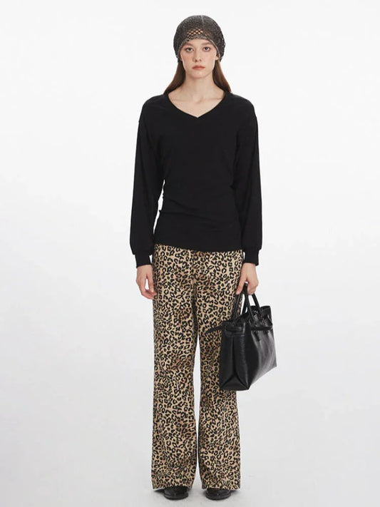 Woman wearing a black V-neck long-sleeved top, leopard print wide-leg pants, a grey knit beanie, and carrying a black structured handbag, shown from the front.