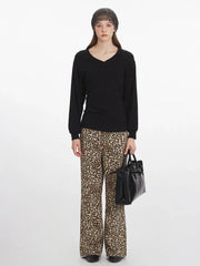 Woman wearing a black V-neck long-sleeved top, leopard print wide-leg pants, a grey knit beanie, and carrying a black structured handbag, shown from the front.