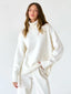 Model wearing an oversized white turtleneck sweater with matching white pants, standing against a white background.