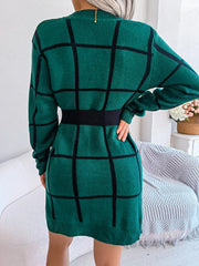 Back view of a woman wearing a green and black plaid knit sweater dress with a black belt