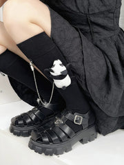 Person wearing knee-high black socks with panda charms and chunky platform sandals