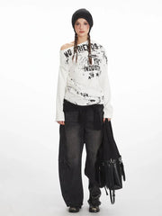 Model wearing a white long-sleeved off-the-shoulder top with distressed graphic print and black wide-leg jeans.