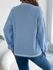 back view of a woman wearing a light blue cable knit v-neck sweater with white stripes and blue jeans