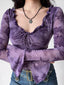 Close-up of a woman wearing a purple sheer mesh top with a floral print, long bell sleeves, and a tie-front detail.