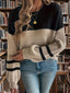 Woman wearing a black and tan color-blocked sweater with striped sleeves and blue jeans, standing in front of a bookshelf.