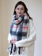 Woman wearing a cream-colored sweater and a plaid scarf, holding the ends of the scarf.