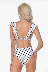 Back view of a woman in a white and black polka dot bikini with ruffled trim and high-waisted bottoms.