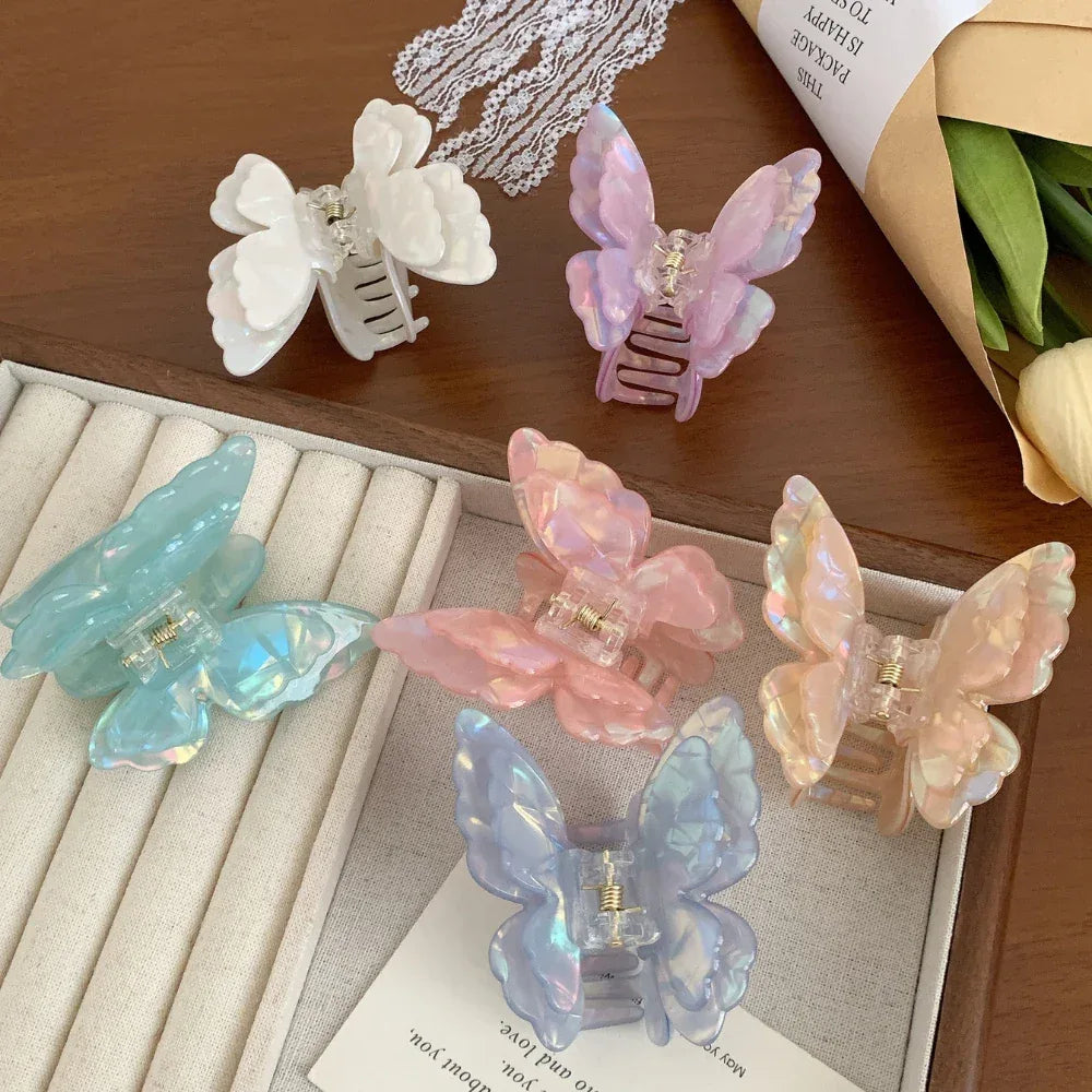Assortment of iridescent butterfly claw clips in different pastel colors displayed in a box and on a tray