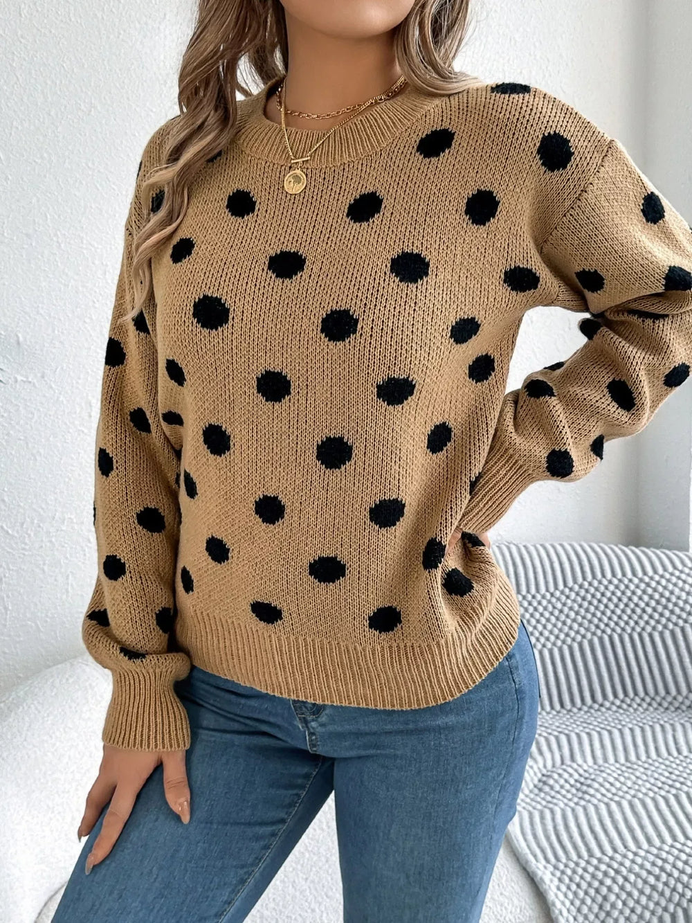 Woman wearing a brown polka dot sweater with blue jeans, side view.