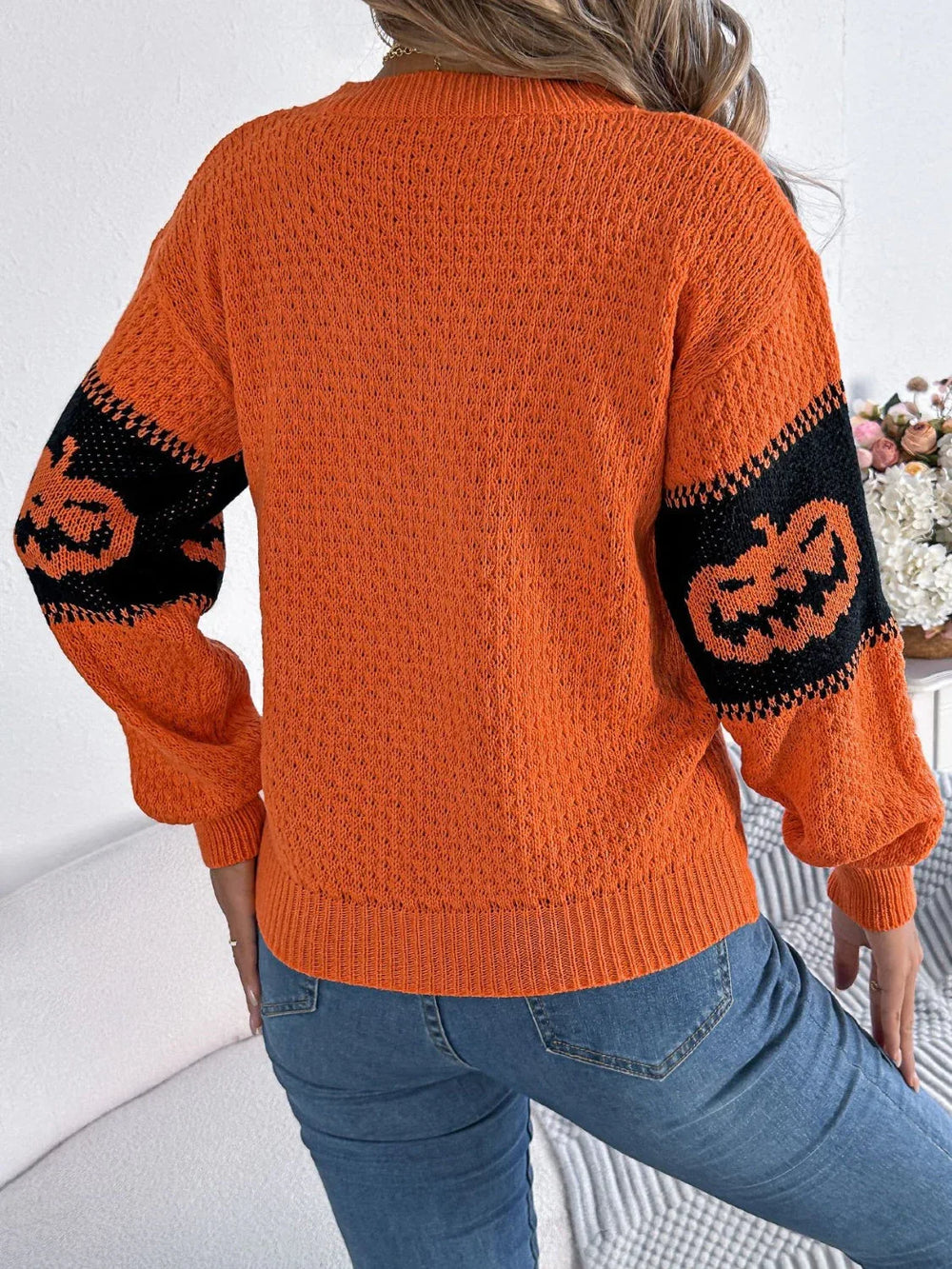 Back view of a woman wearing an orange and black pumpkin print knit sweater