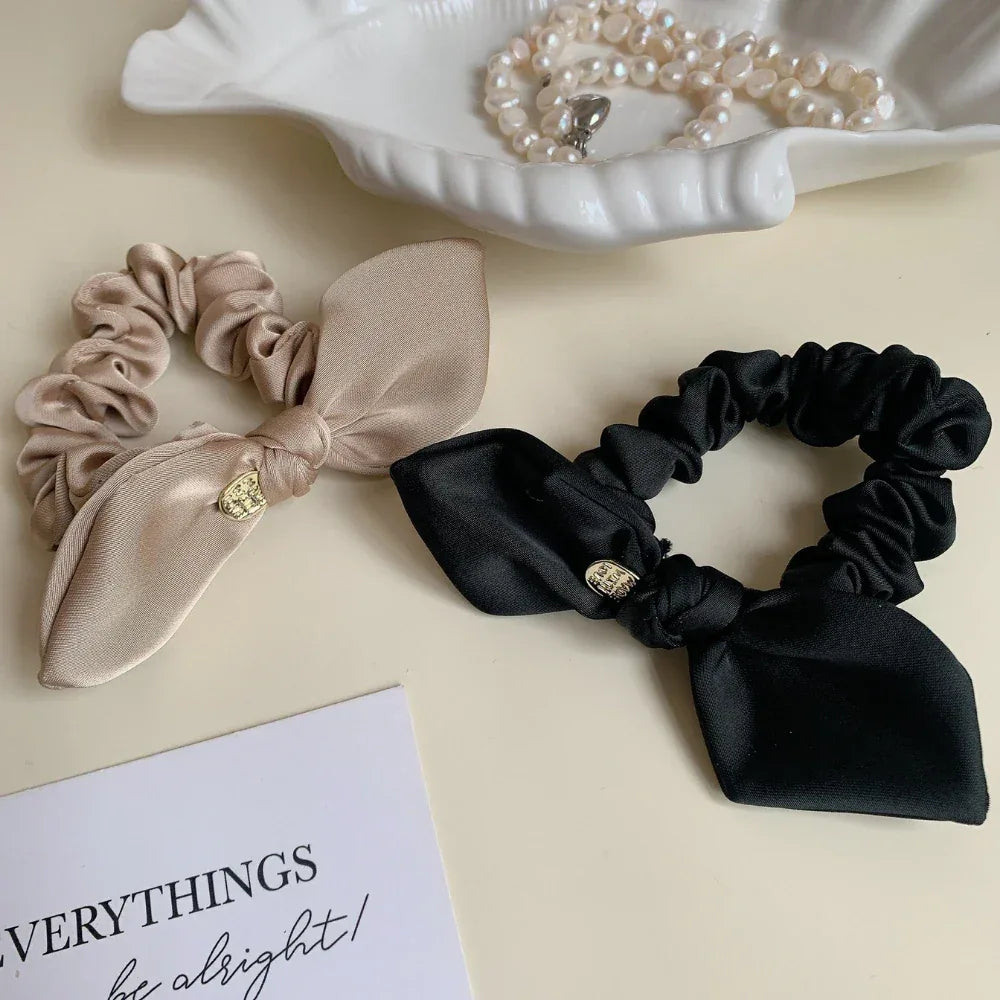 Beige and black satin scrunchies with bow details and gold-tone charms