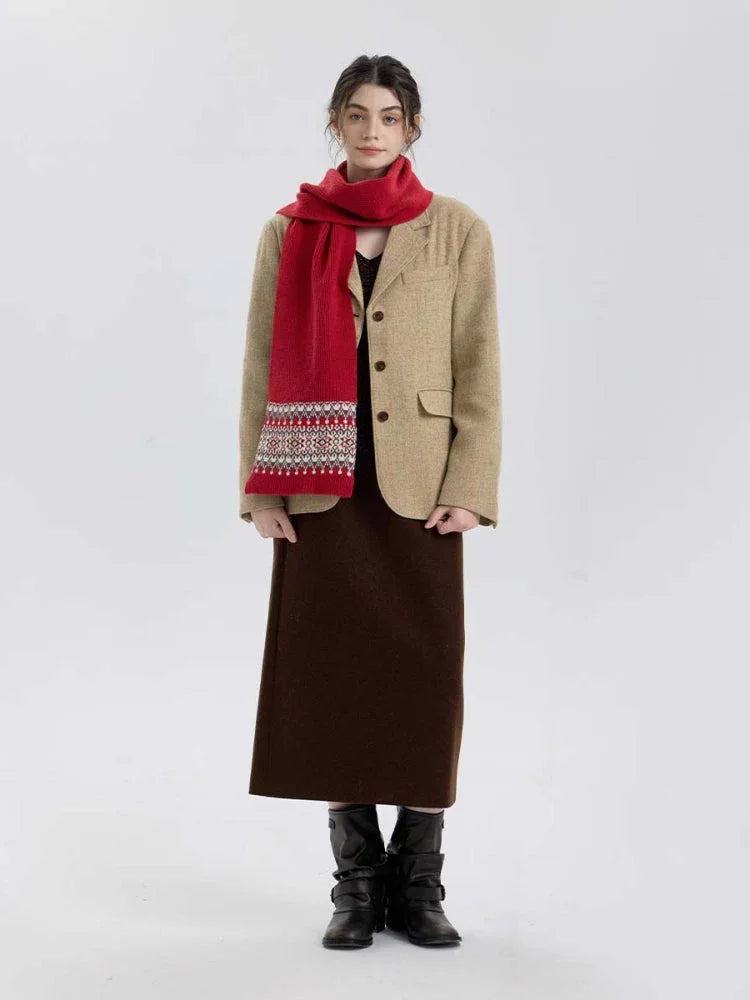 Full body shot of a woman wearing a red knit scarf with a Fair Isle pattern on the ends, over a tan blazer, brown dress, and black boots.