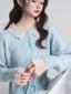 Close-up of a woman's chest and hands wearing a light blue knit cardigan with a white lace collar and cuffs.