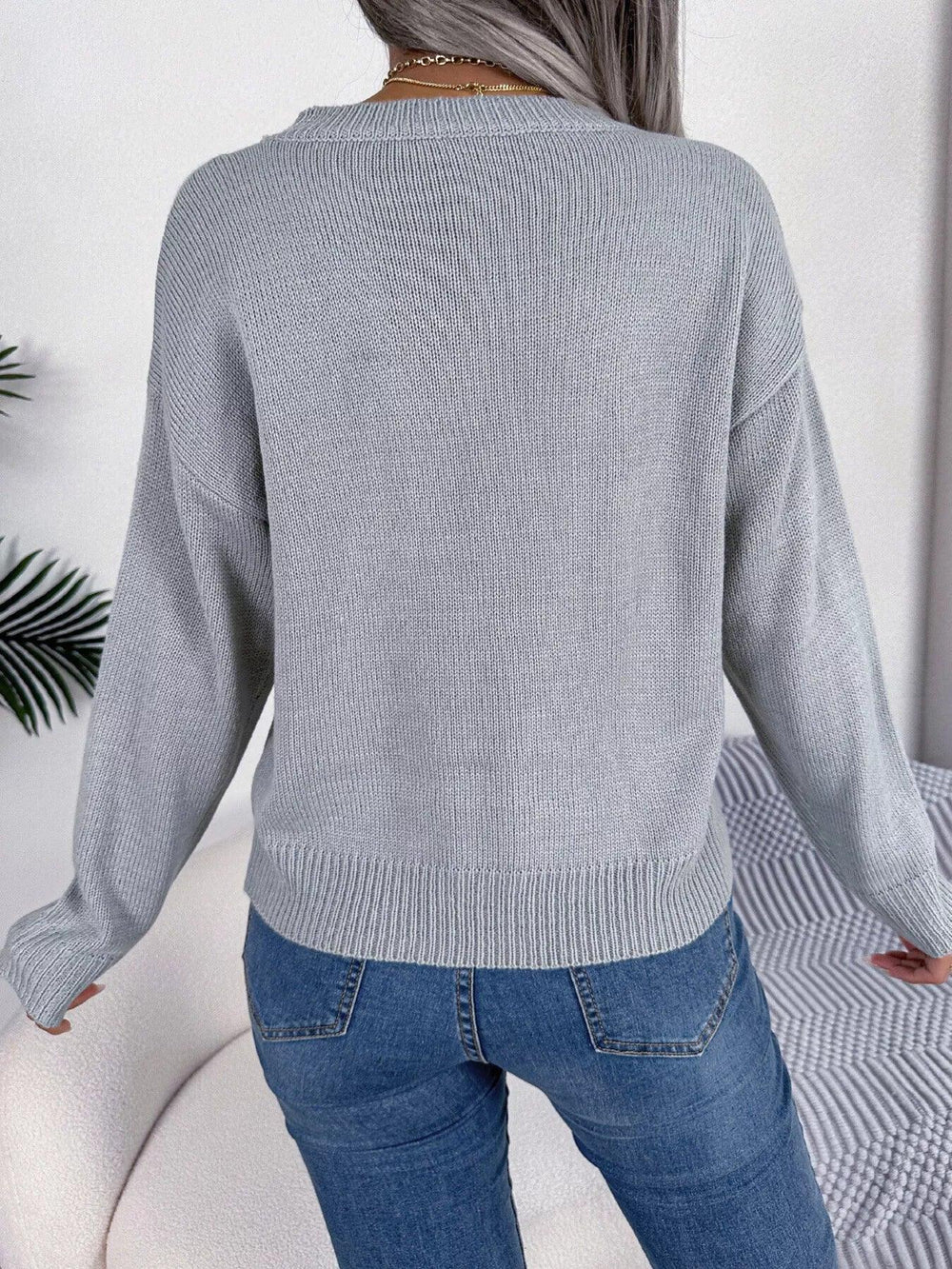 Back view of a woman wearing a grey knit sweater with blue jeans.
