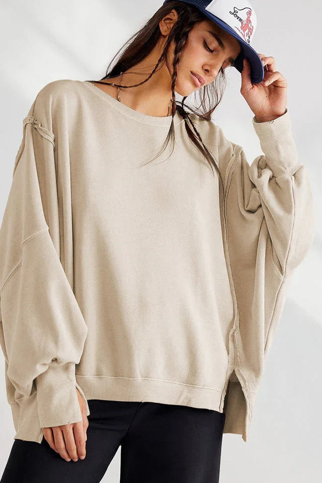 Model wearing a tan oversized sweatshirt with a dropped shoulder and distressed hem, with a baseball cap.