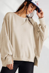 Model wearing a tan oversized sweatshirt with a dropped shoulder and distressed hem, with a baseball cap.