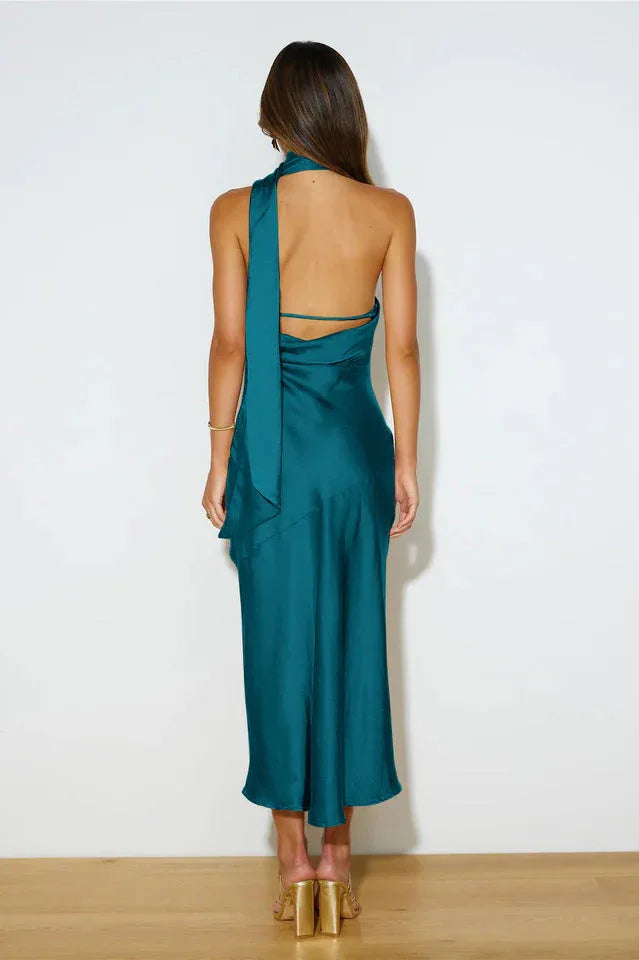 Back view of a woman in a teal satin halter midi dress with a tie detail.