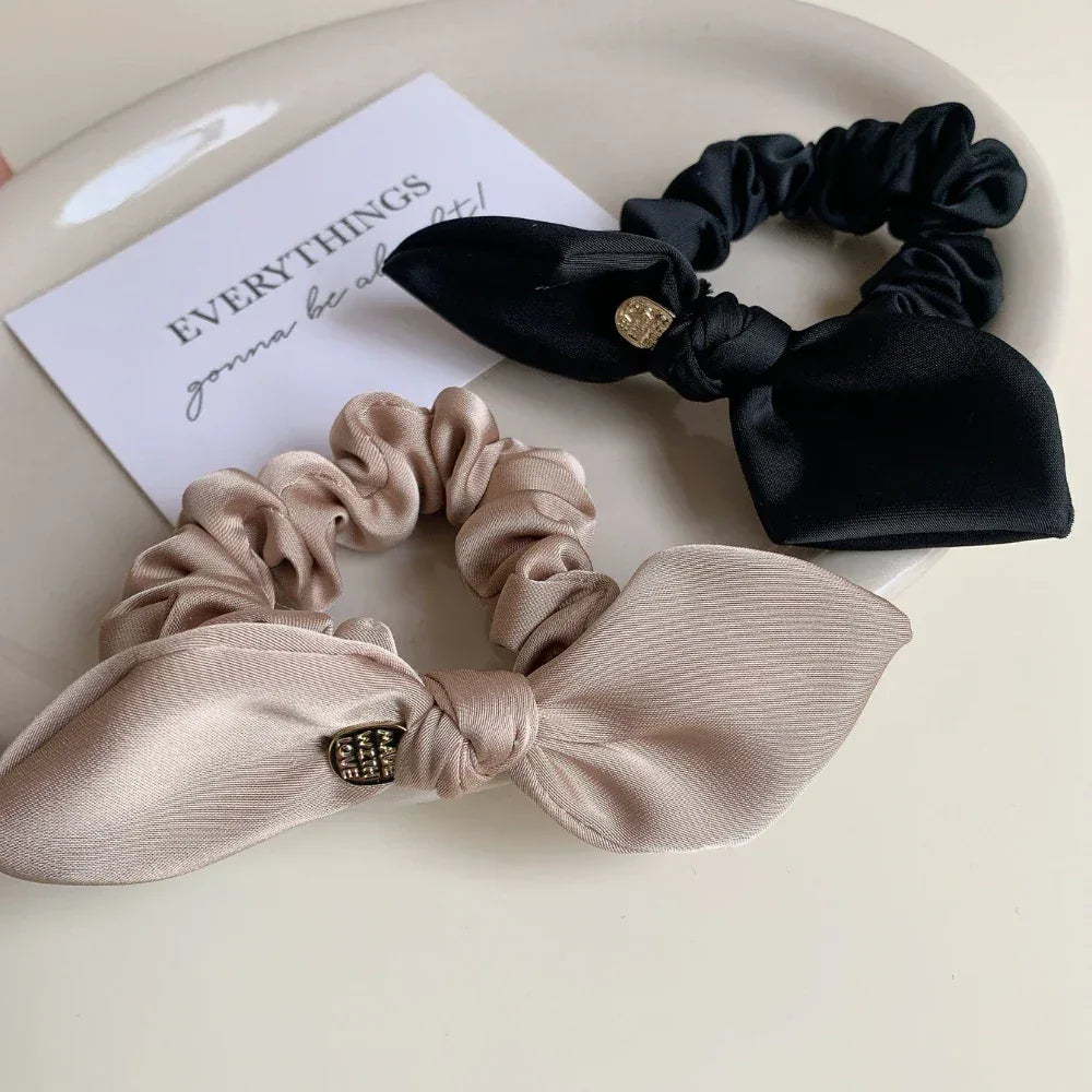 Close-up of beige and black satin scrunchies with bow details and gold-tone charms