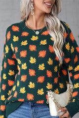 Close-up on the front of a dark green sweater featuring a repeating pattern of orange and yellow maple leaves. The knit texture is visible.