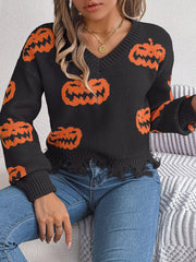 Close-up of a woman wearing a black long-sleeve v-neck cropped knit sweater with an all-over orange pumpkin print and a distressed hem, sitting on a couch.