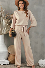 woman wearing a beige wide leg jumpsuit with a tie waist and 3/4 sleeves