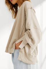 Side view of a model wearing a tan oversized sweatshirt with a dropped shoulder and distressed hem, with hands in pockets.