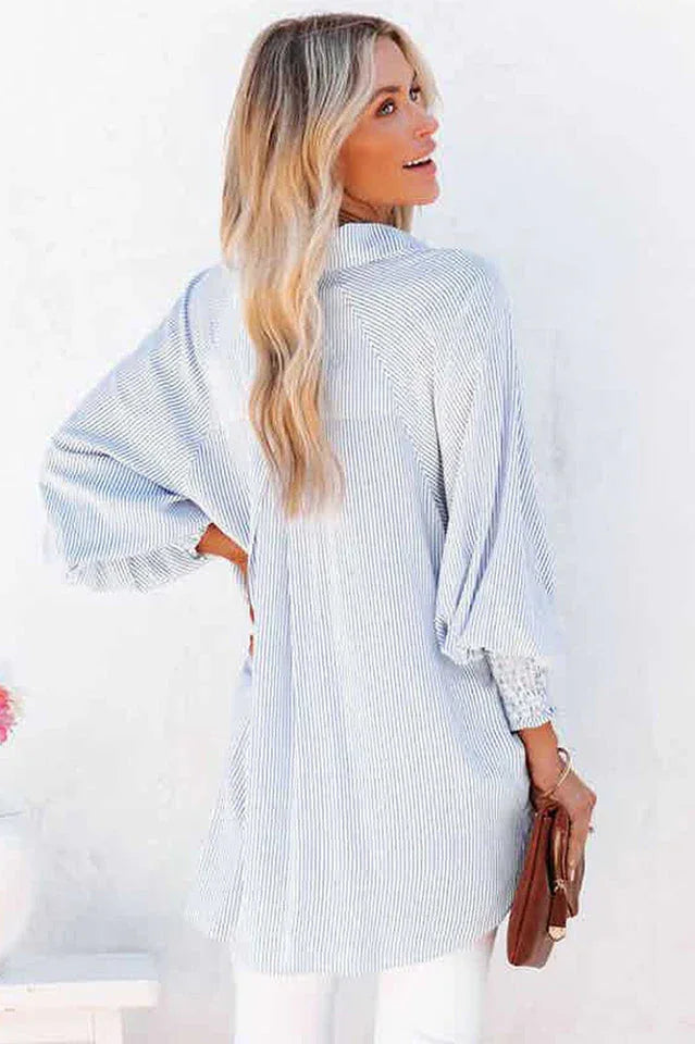 Back view of a woman wearing a white and blue pinstripe oversized button-down shirt with billowing sleeves.