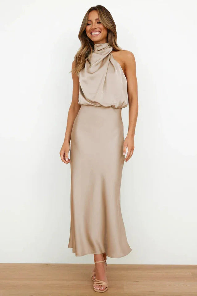 Woman wearing a champagne satin halter neck midi dress, standing against a white background.