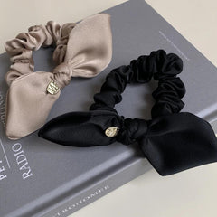 Beige and black satin scrunchies with bow details and gold-tone charms placed on a book