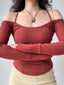 Woman with arms crossed, wearing a rust-colored ribbed knit top with off-the-shoulder long sleeves and a halter neckline.